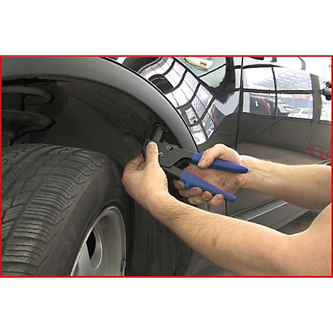 Person repariert Kotflügel. Hände halten Zange mit blauen Griffen. Reifen im Vordergrund, schwarzes Auto.